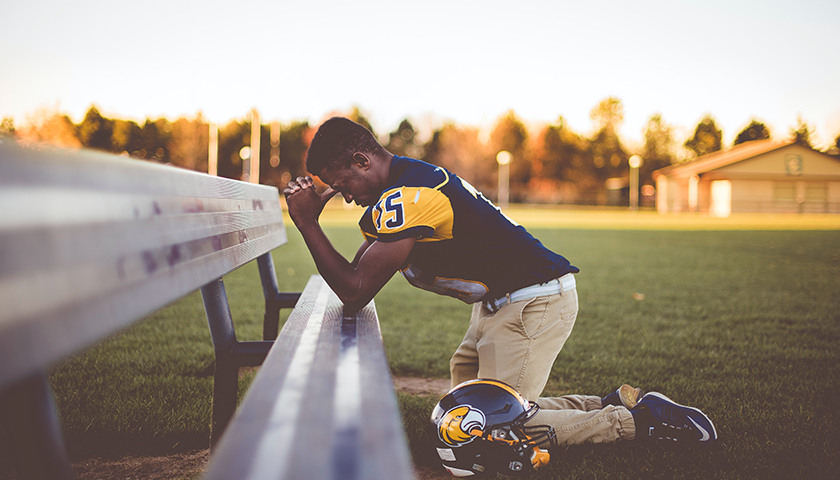 Football player kneeling, praying on bench seat
