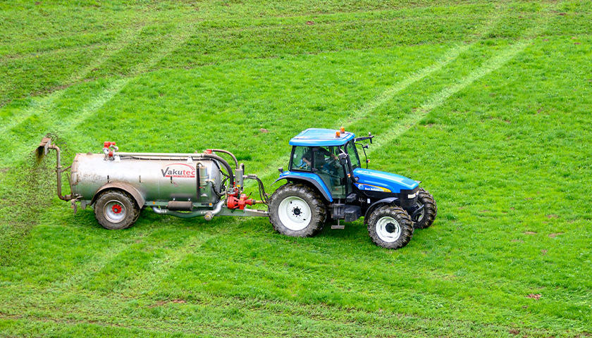 Blue tractor in a field, fertilizing the land